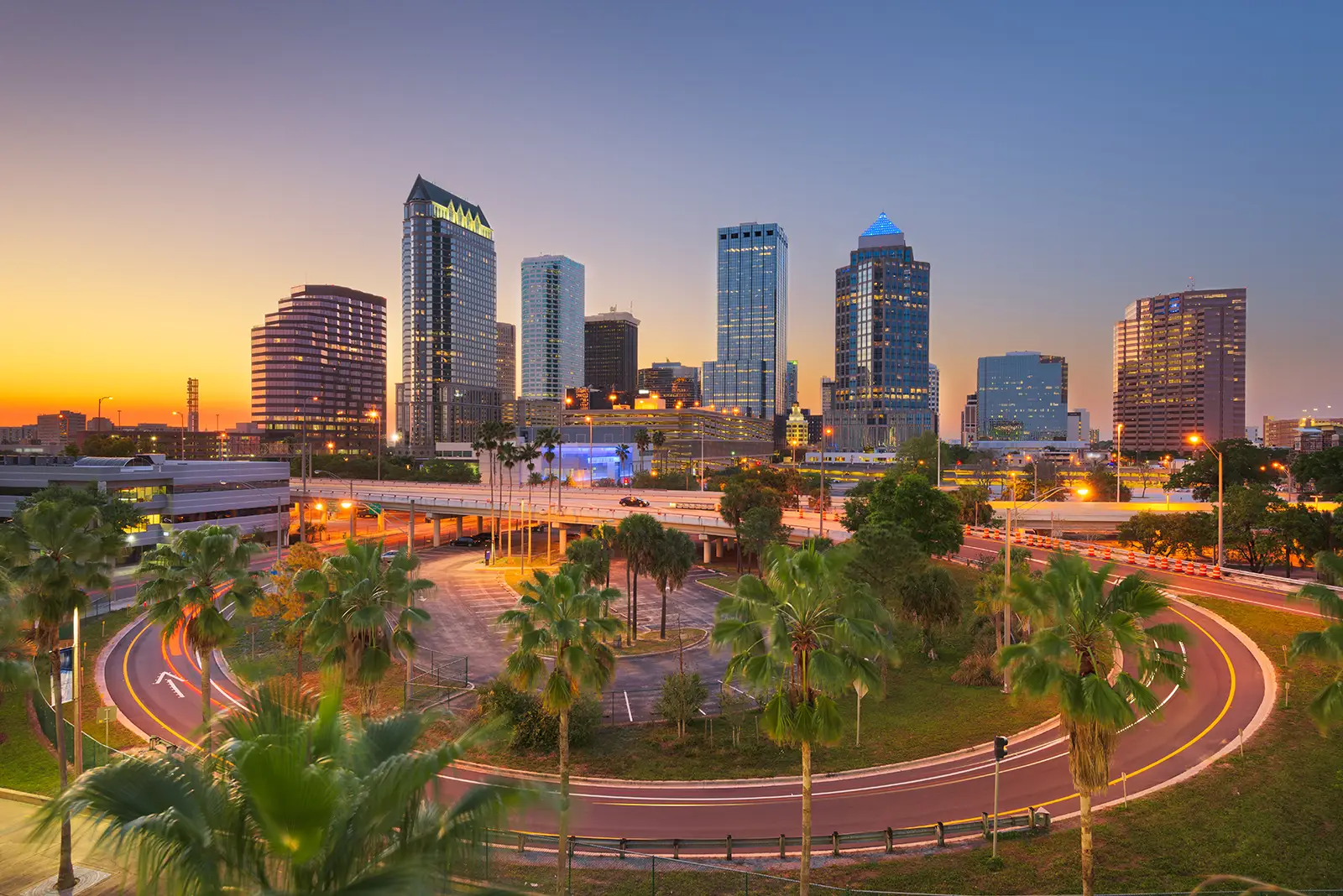 MD Florida Services Skyline von Tampa bei Sonnenuntergang mit Palmen und beleuchteten Straßen